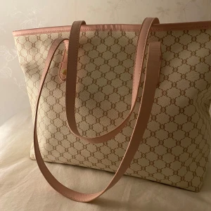 Beige och rosa väska - Säljer en snygg väska i beige med rosa detaljer och ett klassiskt mönster, den köptes från Shein och kan användas till jobbet eller skolan. Väskan har långa axelremmar och är perfekt för att bära med sig allt man behöver. Den har en stilren design som passar till många tillfällen.