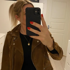 Brun mockajacka i bikermodell från Vero Moda - Snygg brun mockajacka från Vero Moda med dragkedja och stiliga detaljer. Jackan har långa ärmar och en klassisk krage. Perfekt för att ge din outfit en cool touch.