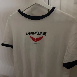 Vit t-shirt från Zadig & Voltaire - Snygg vit t-shirt från Zadig & Voltaire med mörkblå text och röd detalj på framsidan. Baksidan har ett tryck med texten 'L'art donne la liberté d'être jeune'. Nypriset är 1200kr❤️storlek N men känns mer som en s 
