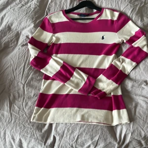 Randig tröja från Ralph Lauren - Säljer en snygg randig tröja från Ralph Lauren i rosa och vit. Tröjan är långärmad och tillverkad i 100% bomull, vilket gör den bekväm och mjuk. Perfekt för en avslappnad stil. 🩷🤍