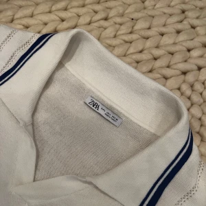 Vit pikétröja från Zara - Säljer en stilren vit pikétröja från Zara med blå ränder på kragen. Jag råkade köpa en för stor storlek. 
