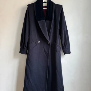 Marin blå  kappa från Michelle Stuart - Elegant marin blå kappa från Michelle Stuart i ullblandning med en stilren design. Den har en djup krage och knäppning framtill. Perfekt för kyligare dagar med sin långa ärm och klassiska look.