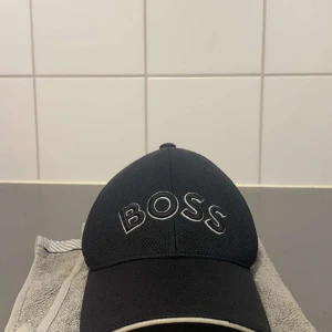 Svart keps från Boss - Snygg svart keps från Boss med broderad logga framtill. Justerbar passform baktill för optimal komfort. Perfekt för en stilren look.  Den är en gång använde pris kan disskuteras vid dm