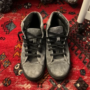 Grå sneakers från Tiger - Snygga grå sneakers från Tiger med svart snörning. Skorna har en stilren design och är tillverkade i mocka. Perfekta för en avslappnad stil. Använda max 2 gånger