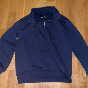 Mörkblå tröja med dragkedja från NO.8 - Säljer en stilren mörkblå half-zip från NO.8 med dragkedja vid halsen. Perfekt för en avslappnad look. Tröjan har långa ärmar och en hög krage.