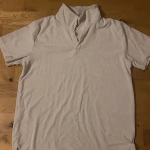 Vit tröja - Säljer en vit frottétröja från Kappahl med korta ärmar och en hög krage. Perfekt för en avslappnad stil. Tröjan är mjuk och bekväm, idealisk för varma dagar. Passar både till stranden och hemma.