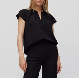 Svart topp från InWear - Säljer en elegant svart topp från InWear. Den har en stilren design med korta ärmar och en v-ringad hals. Perfekt för både vardag och festliga tillfällen. Toppen är i storlek 34 och är i nyskick. Nypris 1200kr