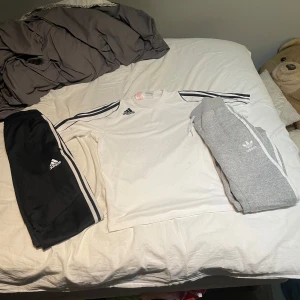 Vit t-shirt från Adidas - Säljer en vit t-shirt från Adidas med klassiska svarta ränder längs ärmarna. Perfekt för sport och träning. T-shirten har en normal passform och är kortärmad. Adidas T-shirt 140cm Adidasbyxor byxor svarta 152cm adidas byxor grå 140cm