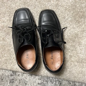 Svarta skor från Auston - Snygga svarta skor från Auston med snörning och fyrkantig tå. Skorna har en robust sula och är tillverkade i skinn, vilket ger en klassisk look. Perfekta för en stilren och elegant stil.