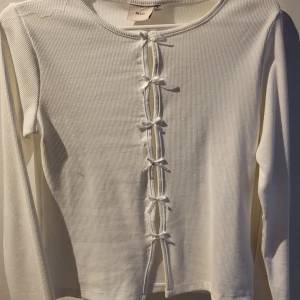 Vit ribbad topp från Nelly - Säljer en stilren vit ribbad topp från Nelly med långa ärmar och knytning framtill. 
