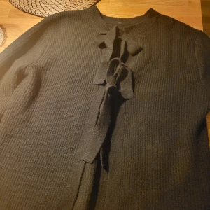 Svart stickad tröja från Pieces - Säljer en stilren svart stickad tröja från Pieces. Tröjan har en knytning framtill som ger en fin detalj.