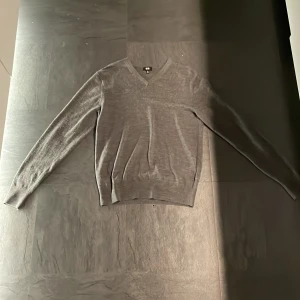 Mörk Grå tröja från Uniqlo - Säljer en stilren mörk grå tröja från Uniqlo i storlek XS. Tröjan har en v-ringad design och är tillverkad i ett mjukt material som passar perfekt för kyligare dagar. Perfekt för dig som gillar en klassisk look. Köpt på uniqlo. Har ett litet hål i vänster armhåla.