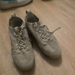 Beige Nike sneakers - Säljer ett par beige Nike sneakers med stickad ovandel och snörning. Skorna har en modern design med en bekväm passform och är perfekta för vardagsbruk.