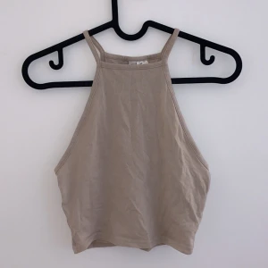 Beige ärmlös linnetopp - Säljer en stilren beige linnetopp i mycket bra skick. Toppen är ärmlös med en hög halslinje och smala axelband. Perfekt för sommardagar eller som ett basplagg i garderoben. Passar till både jeans och kjol!
