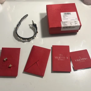 Valentinoarmband  - Säljer ett coolt grått armband från Valentino med guldiga nitar. Armbandet är i skinn och har en justerbar spänne för perfekt passform. Kommer med originalförpackning och certifikat. Perfekt för att ge din outfit en modern touch!nypris runt 3000kr