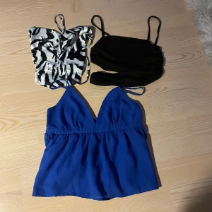 Toppar - Säljer tre sommartoppar, alla tillsammans. En blå topp med v-ringning och smala justerbara axelband. En svart topp med smala axelband och slits över magen. Den tredje är en mönstrad topp med zebra-mönster som går att knyta i ryggen