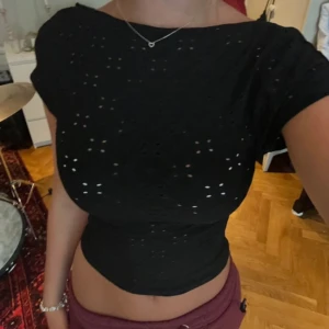 Svart kortärmad topp med öppen rygg - Säljer en svart kortärmad topp med ett coolt hålmönster och öppen rygg. Perfekt för sommarens fester eller en utekväll. Toppen är tight och croppad, vilket ger en snygg och trendig look. Passar bra till både jeans och kjol!