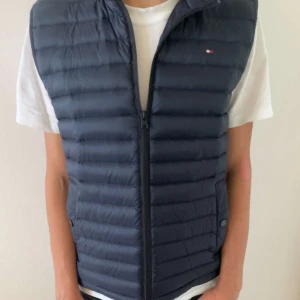 dunväst från Tommy Hilfiger - Säljer en snygg mörkblå dunväst från Tommy Hilfiger i storlek XS men passar som S också. Den är i mycket bra skick använd max 3 gånger. Nypris cirka-1500 mitt pris 300. Den kmr med sin egna påse där man kan lägga västen i
