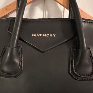 Säljer en elegant svart skinnväska från Givenchy i mycket bra skick. Väskan har både handtag och en avtagbar axelrem, vilket gör den perfekt för både vardag och fest. Insidan är rymlig med en dragkedjeficka för extra säkerhet. En tidlös design som passar alla säsonger. Dragkedjan är sönder, men annars i väldigt gott skick. 