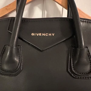 Svart skinnväska från Givenchy - Säljer en elegant svart skinnväska från Givenchy i mycket bra skick. Väskan har både handtag och en avtagbar axelrem, vilket gör den perfekt för både vardag och fest. Insidan är rymlig med en dragkedjeficka för extra säkerhet. En tidlös design som passar alla säsonger. Dragkedjan är sönder, men annars i väldigt gott skick. 