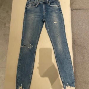 Jeans med slitningar - Säljer ett par snygga blå jeans med slitningar på framsidan. De är midwaist och har en tight passform.