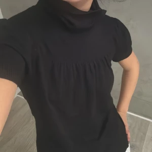 Svart polotopp - Säljer en stilren svart polotopp med korta ärmar. Toppen har en bekväm passform. 