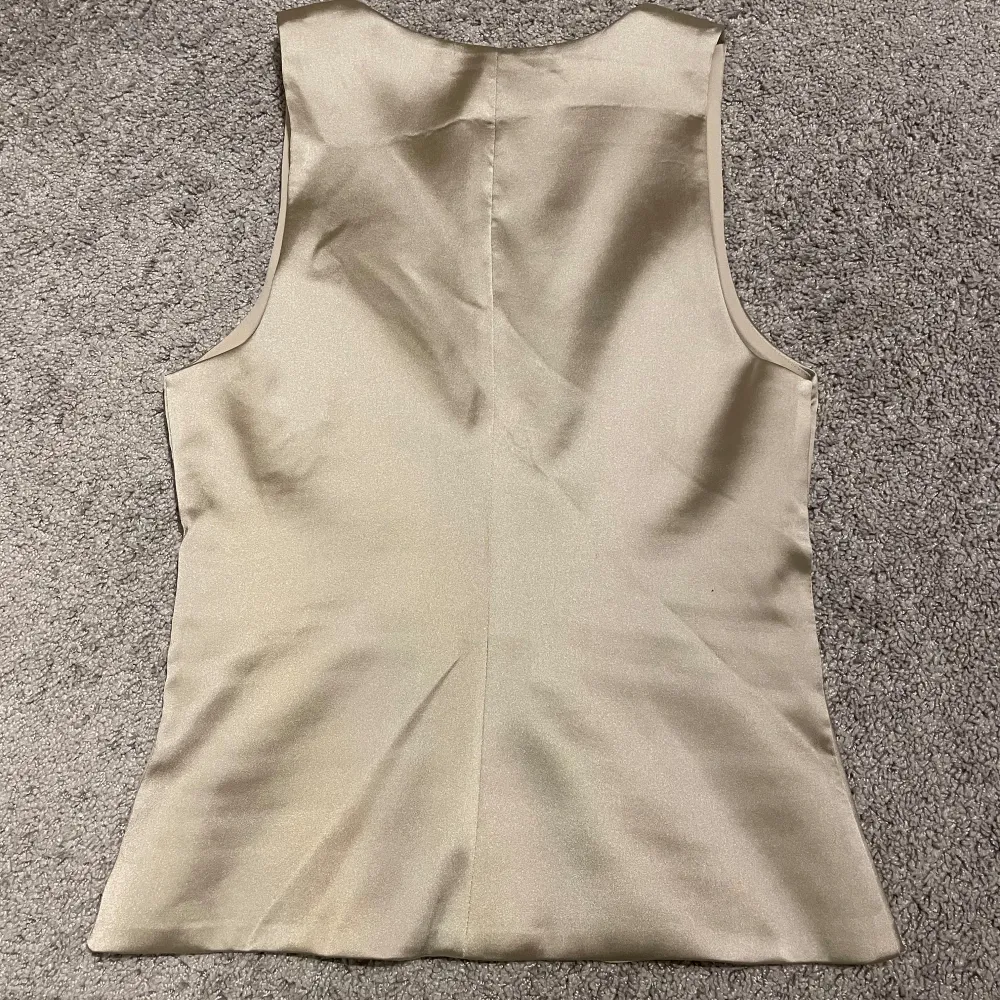 Säljer en stilren beige väst från Zara i storlek XS. Västen har en elegant v-ringning och är perfekt för både fest och vardag. Materialet är mjukt och ger en lyxig känsla. Passar utmärkt till både jeans och kjol. Helt ny med taggar kvar!. Toppar.