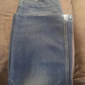 Blå jeansbyxor - Säljer ett par vida  blå jeans i bra skick. . Jeansen har en traditionell femficksdesign och är tillverkade i slitstarkt denim.  Tror att jag har kortar ner till till 32 från 34