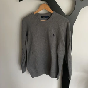 Grå tröja från Polo Ralph Lauren - Säljer en stilren grå tröja från Polo Ralph Lauren i storlek L, men passar s-m. Tröjan är i nyskick och har en klassisk design med rund hals. Modellen på bilden är 183cm 80kg. Nypris 1400kr