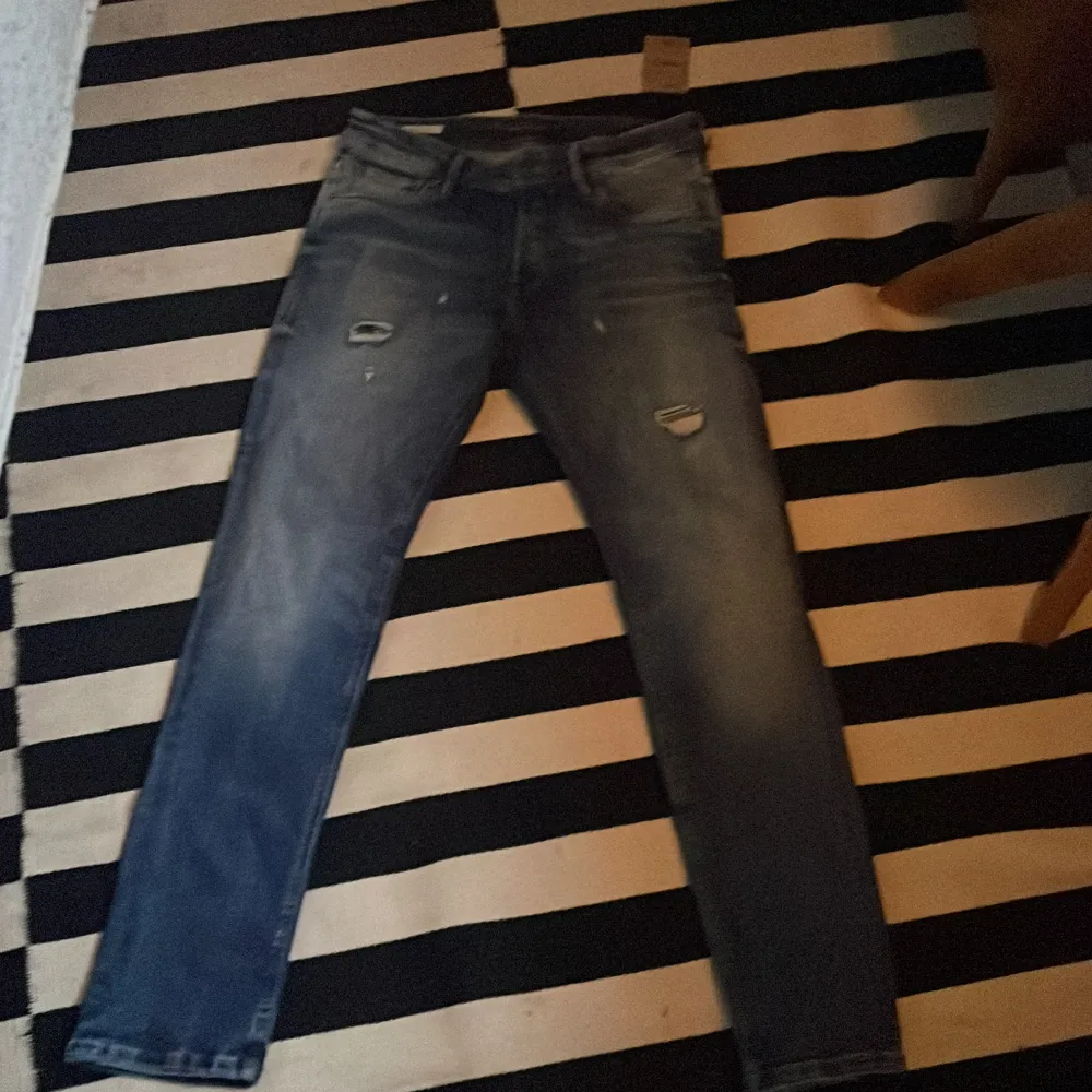 Säljer ett par snygga blå jeans från Jack & Jones i slim fit. De har en cool slitning på framsidan som ger en avslappnad look. Perfekta för både vardag och fest! 🕺. Jeans & Byxor.