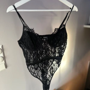 Svart spetsbody - Snygg svart spetsbody från NA-KD med tunna axelband och vacker spetsdetalj. Perfekt för en utekväll eller fest. Den har en elegant och sexig design som framhäver figuren. Ett måste i garderoben för speciella tillfällen!