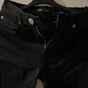 Svarta jeans från Zara - Säljer ett par snygga svarta jeans från Zara. De har en klassisk design med dragkedja och knapp framtill och slits där nere. Perfekta för både vardag och fest! 🖤