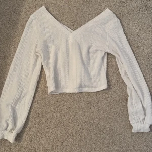 Vit v-ringad blus - Säljer en stilren vit blus med v-ringning och långa ärmar. Blusen har en lätt textur och är perfekt för både vardag och fest. Den är croppad och ger en modern look. Passar bra till jeans eller kjol🍂🧡