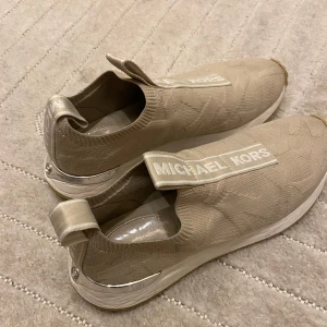 Beige sneakers från Michael Kors - Snygga beige sneakers från Michael Kors. De har en stilren design med logotypen på ovansidan och en silvrig detalj vid hälen. Superbekväma att bära. Passar till både vardag och fest!