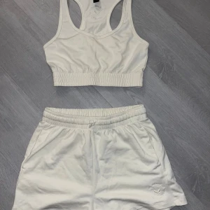 Vit träningstopp och shorts från SOC - Säljer ett set med vit träningstopp och matchande shorts från SOC. Toppen är ärmlös med en tight passform och elastisk midja. Shortsen har en bekväm resår i midjan. Perfekt för träning eller en avslappnad dag. Båda delarna är i mycket bra skick!