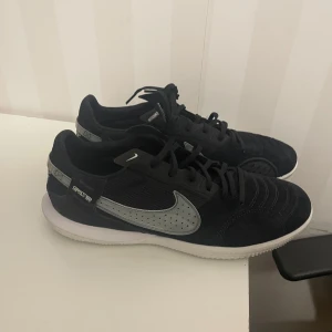 Inomhusskor fotboll  - Säljer ett par snygga svarta sneakers med silverdetaljer. De har en cool design med snörning och en bekväm passform. Perfekta för både vardag och träning. Skorna är i mycket bra skick och redo för nya äventyr!