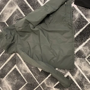 Grön vinterjacka med huva - Säljer en grön vinterjacka med huva och foder. Jackan har dragkedja och knappar framtill samt två snedställda bröstfickor med dragkedja. Perfekt för kalla dagar! 🧥