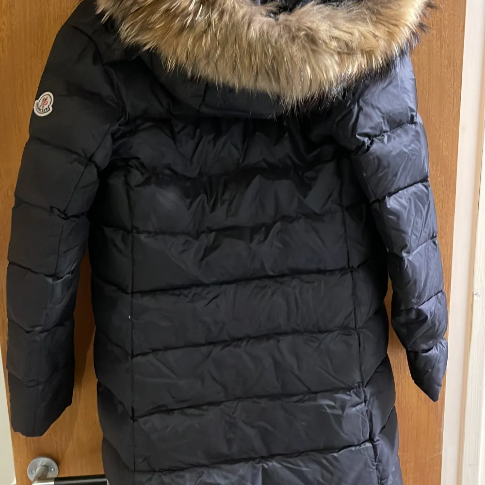 Säljer en snygg svart dunjacka från Moncler med pälskantad huva som även är avtagbar. Jackan är perfekt för kalla vinterdagar och har en stilren design med dragkedja framtill. Den är i använt skick med ett fåtal defekter. Men är en väldigt fin jacka från moncler. . Jackor.