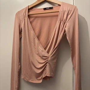 Rosa omlottopp från Boohoo - Säljer en superfin rosa omlottopp från Boohoo i storlek S. Toppen är i ett mjukt och stretchigt material av polyester och elastan. Den har långa ärmar och en snygg v-ringning. Perfekt för både vardag och fest!