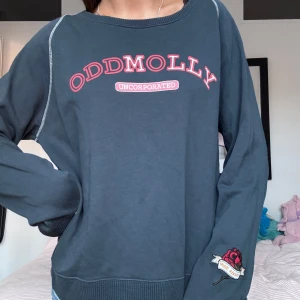 Mörkblå sweatshirt från Odd Molly - Säljer en snygg mörkblå sweatshirt från Odd Molly med coolt tryck på bröstet och en rosdetalj på ärmen. Perfekt till skolan 