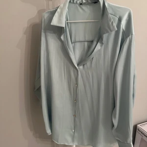 Mintgrön blus Zara - Säljer en elegant ljusblå blus i ett mjukt och lätt material. Blusen har långa ärmar och knappar framtill, vilket ger en klassisk look. Perfekt för både vardag och festliga tillfällen. Passar bra till jeans eller kjol för en stilren outfit.  Använd sparsamt. Storlek xxl(tänk på zaras storlekar) 
