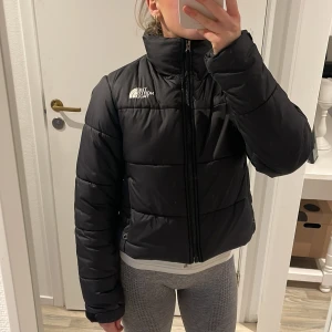 The North Face jacka - OBS!! Fläckarna på bilden är på spegeln, inte på jackan. — Säljer en svart jacka från The North Face i mycket bra skick. Jackan är perfekt för kalla dagar med sin pufferstil och dragkedja framtill samt vid fickor. Den har en hög krage för extra värme och är långärmad. Passar perfekt för både höst och vinter!