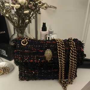 väska kurtgeiger  - Säljer en superfin axelväska från Kurt Geiger i modellen The Kensington. Väskan har ett unikt flerfärgat mönster med inslag av rött, blått och svart. Den har en elegant kedja i guld och en snygg detalj framtill. Perfekt för att liva upp vilken outfit som helst! den är i nyskick utan någon deffekt!