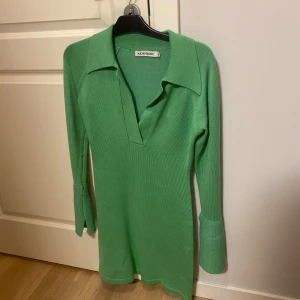 Grön stickad klänning från Adoore - Säljer en superfin grön stickad klänning från Adoore. Den har en djup v-ringning och långa ärmar med ribbade detaljer. Perfekt för höst och vår, och den är både bekväm och stilren. 