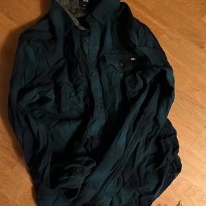 Mörkgrön skjorta från Vans - Säljer en snygg mörkgrön skjorta från Vans i bra skick. Skjortan har långa ärmar och knappar framtill. Perfekt för höst och vår, och funkar både till vardags och fest. Skön och stilren design som passar till det mesta. Hör av dig vid intresse!