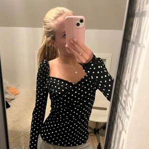Svart prickig omlottopp - Säljer en superfin svart omlottopp med vita prickar. Toppen har långa ärmar och en smickrande omlottdesign som ger en elegant look. Perfekt för både vardag och fest! 🖤storleken syns inte i lappen men skulle säga S-M