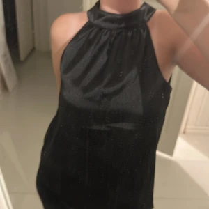 Svart glansig blus - Snygg svart glansig jätte snygg blus med hög hals och ärmlös design. Perfekt för festliga tillfällen och nyårsfirande. Har aldrig använt den bara testat. Inga defekter.