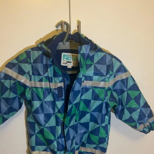 Mönstrad jacka från MyWear Active - Säljer en cool jacka från MyWear Active i storlek barn XL. Den har ett geometriskt mönster i blått och grönt med reflexdetaljer. Perfekt för höst och vår med sitt fleecefoder som håller värmen. Jackan har dragkedja och är långärmad. Perfekt för aktiva dagar utomhus!