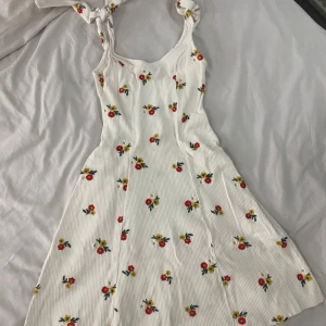 Vit blommig klänning med knytband - Säljer en superfin vit klänning med färgglada blommor och knytband på axlarna. Perfekt för sommardagar och midsommarfirande! Klänningen har en lätt och luftig passform med en söt blommig design. Den är i mycket bra skick och redo för nya äventyr. 🌸