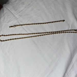 Guldfärgat halsband och armband - Säljer ett snyggt set med guldfärgat halsband och matchande armband. Båda har en vriden design som ger en elegant touch. Perfekt för att piffa upp vilken outfit som helst, oavsett om det är till vardags eller fest. Låset är enkelt att använda och håller smyckena säkert på plats.